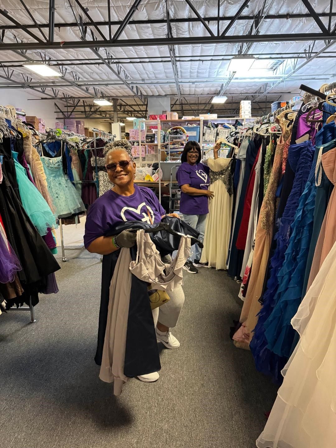A member in a purple shirt sorting donated dresses on clothing racks
