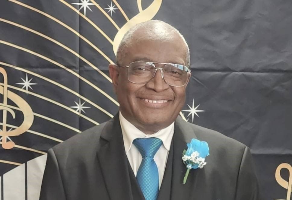 Rev. Dr. Rickey E. Williams, smiling, in a dark suit with a blue boutonniere